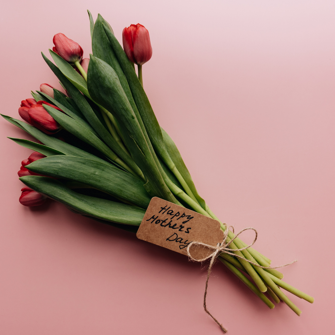 Bouquet of red tulips with a handwritten tag that reads “Happy Mother’s Day” on a pink background