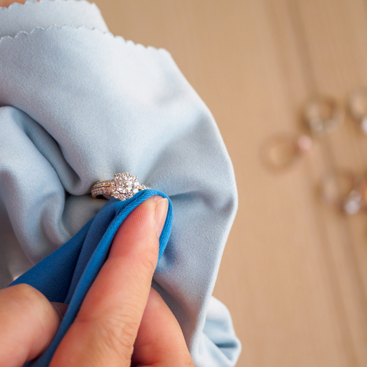 Hand cleaning a diamond ring with a soft polishing cloth to maintain its sparkle.