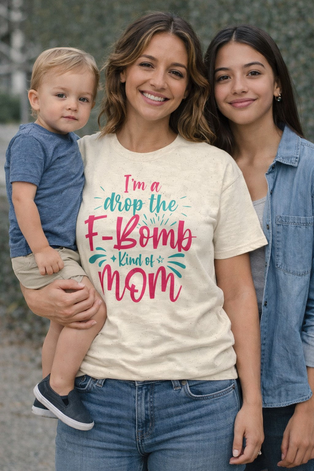 Mom wearing “I’m a Drop the F-Bomb Kind of Mom” t-shirt while holding her child, a funny and relatable motherhood moment.