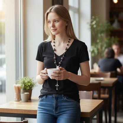 Woman in black t-shirt and jeans holding coffee, wearing a Jena Jewelry rosary with black obsidian and floral lampwork beads.