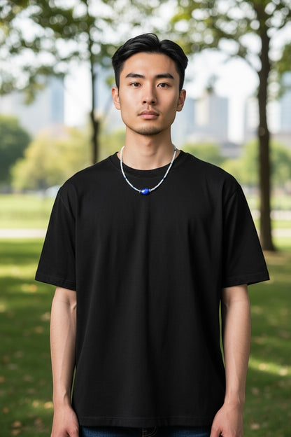 Jena Jewelry men's seed bead necklace with a large blue stone pendant and white beads, worn with a black t-shirt.