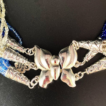 Jena Jewelry multi-strand braided glass seed bead necklace with silver butterfly clasp and ornate end caps. Blue and clear beads.