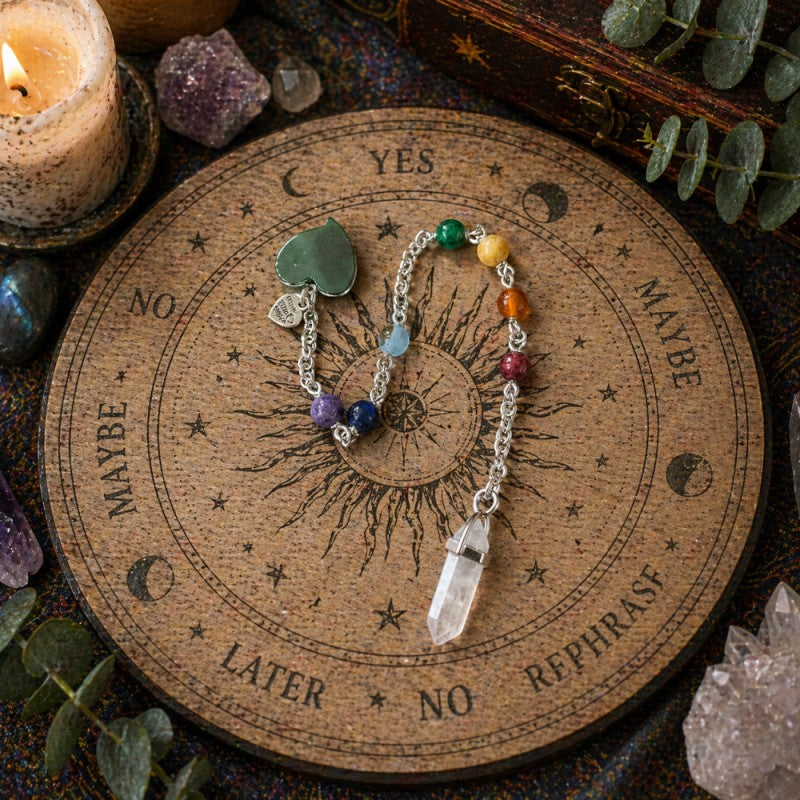 Jena Jewelry chakra healing pendulum with hematite heart, gemstone beads, and rose quartz point on a wooden divination board.