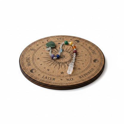 Jena Jewelry chakra healing pendulum with hematite heart, gemstone beads, and rose quartz point on a divination board.