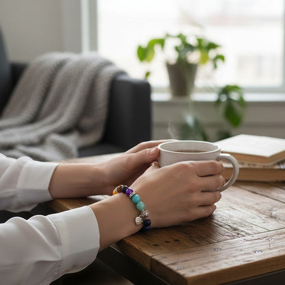 Jena Jewelry Chakra Stretch Bracelet with colorful beads including amethyst, lapis, aventurine, tiger eye, and jade, worn by a woman holding a steaming mug.