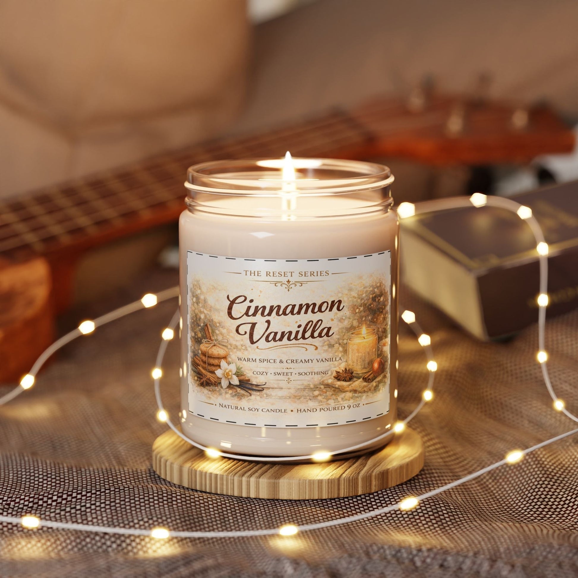 Jena Jewelry Cinnamon Vanilla natural soy candle in a glass jar with a black lid, lit and surrounded by fairy lights.