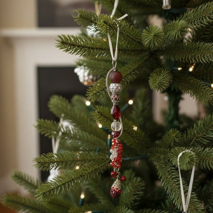 Jena Jewelry handcrafted festive icicle ornament with red and silver glass beads, charms, and jingle bells hanging on a Christmas tree.