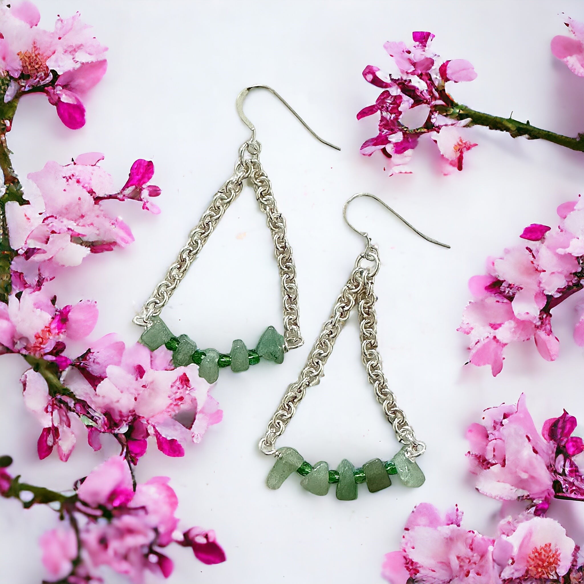 Jena Jewelry green aventurine and crystal quartz chainmaille earrings with silver metal accents, framed by pink blossoms.