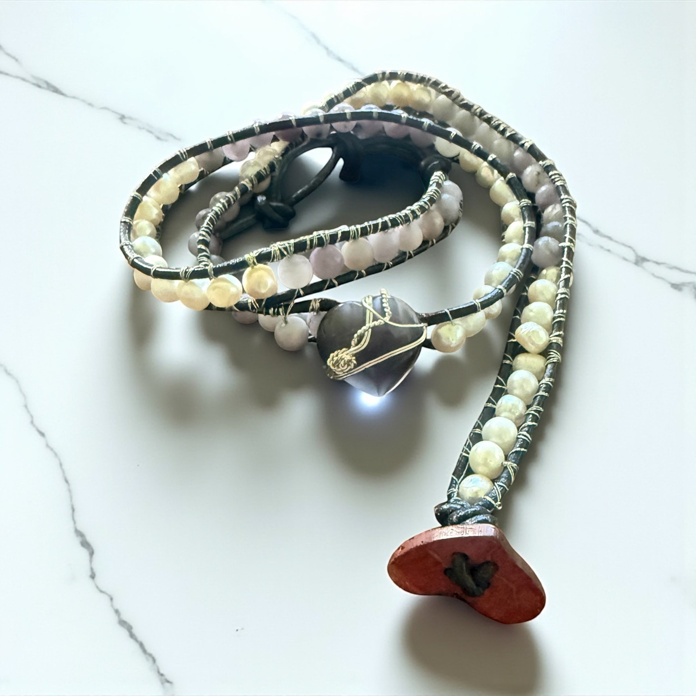 Jena Jewelry leather-wrapped bracelet with freshwater pearls, amethyst beads, and coconut button clasp. Features a heart-shaped amethyst pendant.