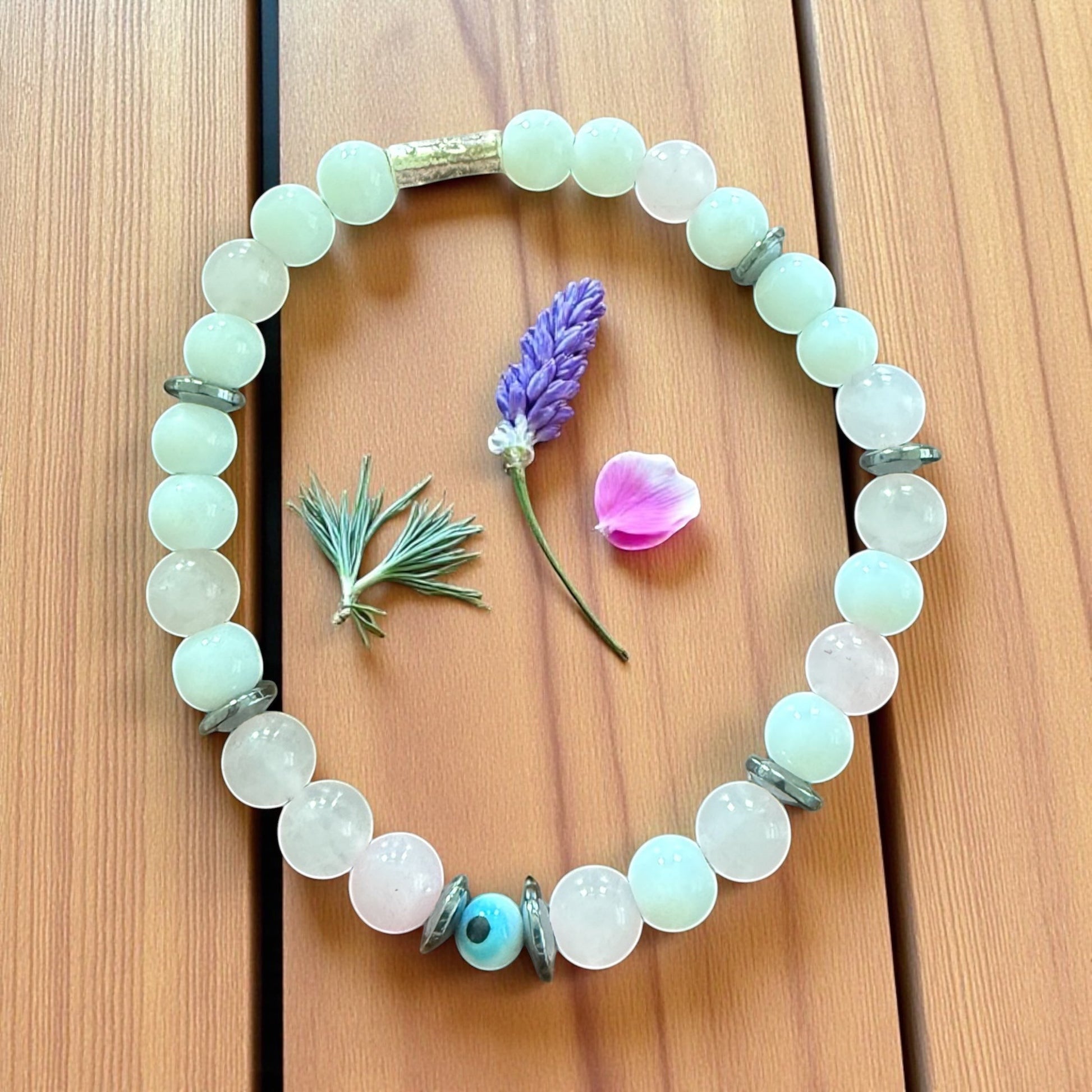 Jena Jewelry bracelet with light green jade, rose quartz, and hematite beads spelling 'F*ck Off' in Morse code. Features a central blue evil eye bead.