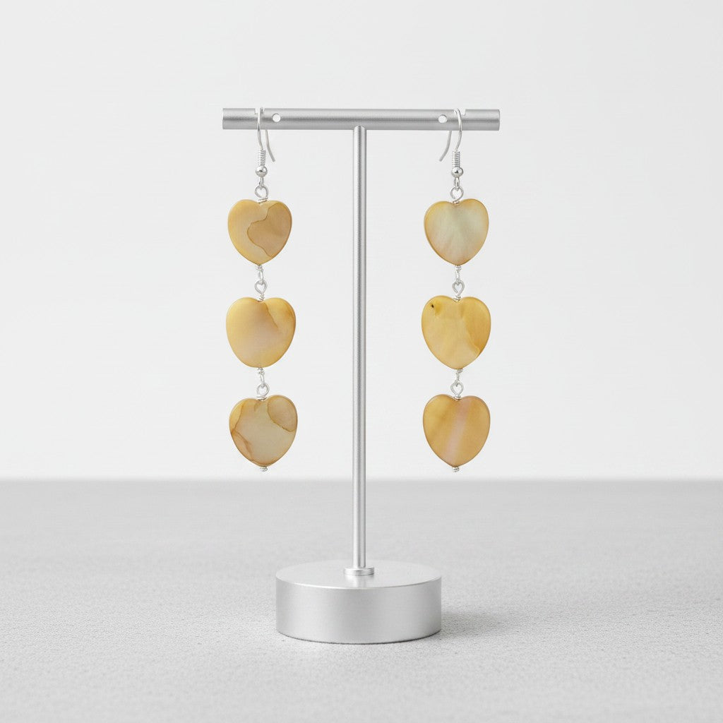 Jena Jewelry tea-dyed mother of pearl heart dangle earrings in warm, iridescent tones with silver hooks.