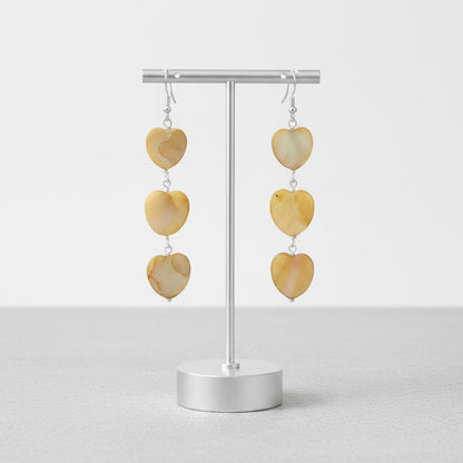 Jena Jewelry tea-dyed mother of pearl heart dangle earrings in warm, iridescent tones with silver hooks.