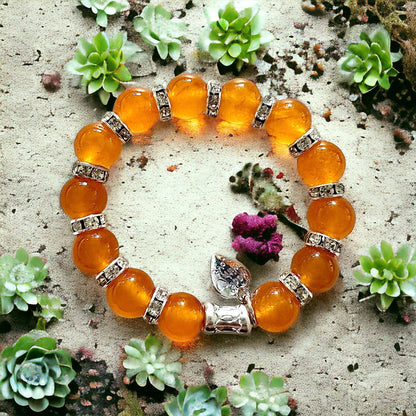 Jena Jewelry orange jade beaded bracelet with rhinestone spacers and a silver charm, set against a sandy background with succulents.