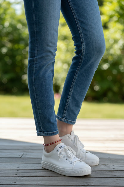 Jena Jewelry handmade red seed bead anklet with silver accents on a woman's ankle, worn with blue jeans and white sneakers.