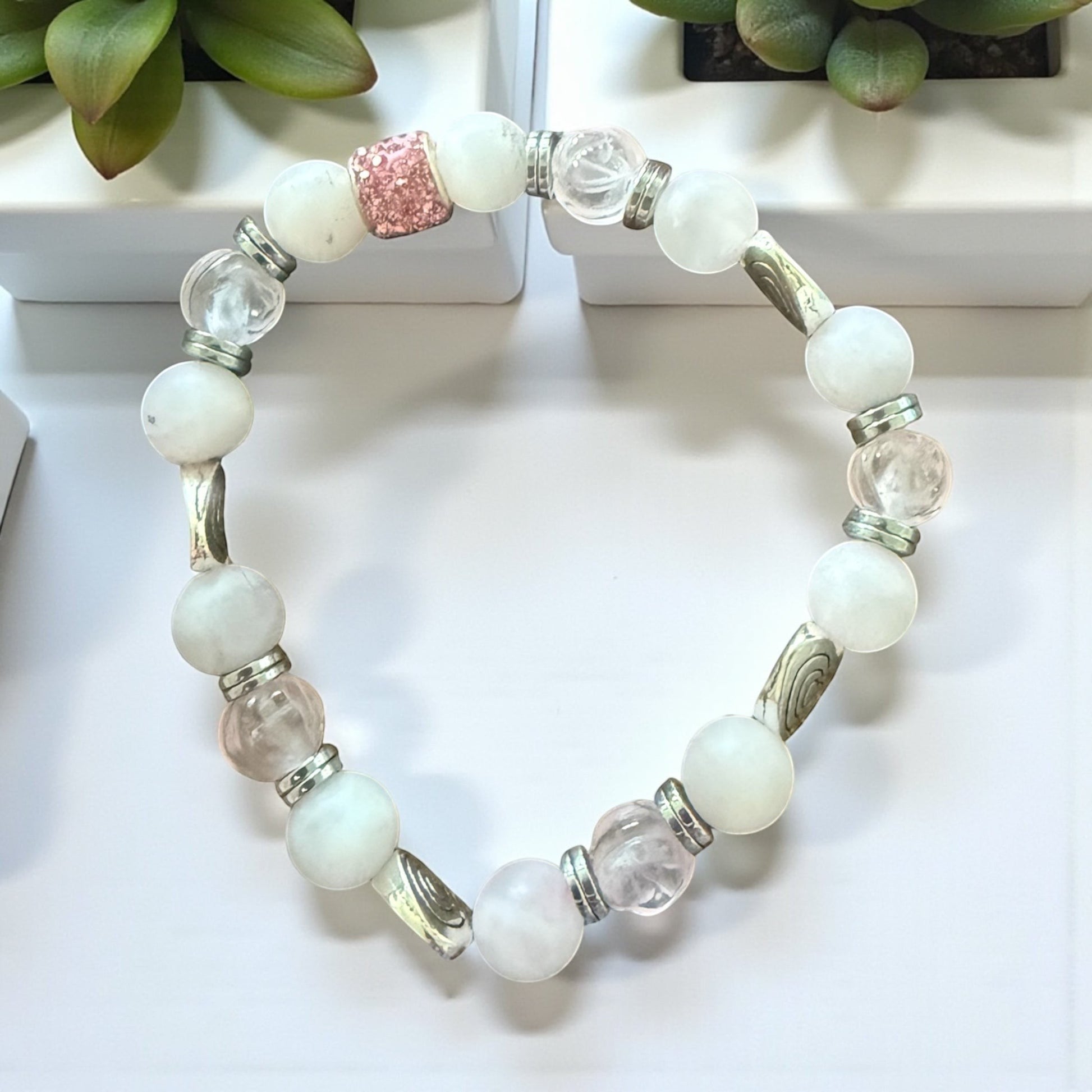 Jena Jewelry stretch bracelet with rose quartz, snow jade, clear glass beads, and silver heart accents. Features a pink glitter bead.
