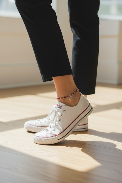 Jena Jewelry handmade seed bead anklet with red, black, and white beads and a heart charm, worn with white sneakers.