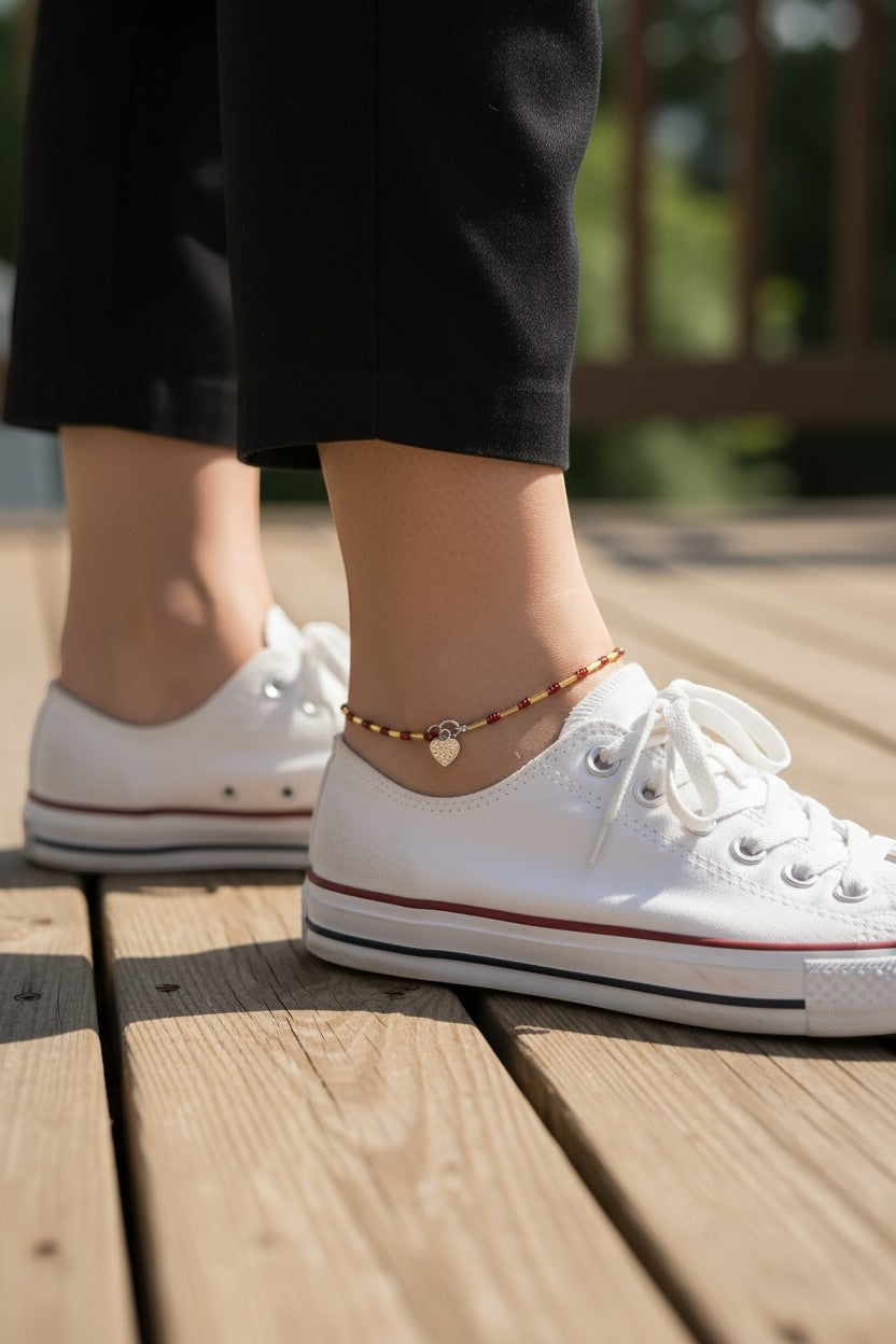 Jena Jewelry handmade seed bead anklet with red beads, gold accents, and a heart charm, worn with white sneakers.