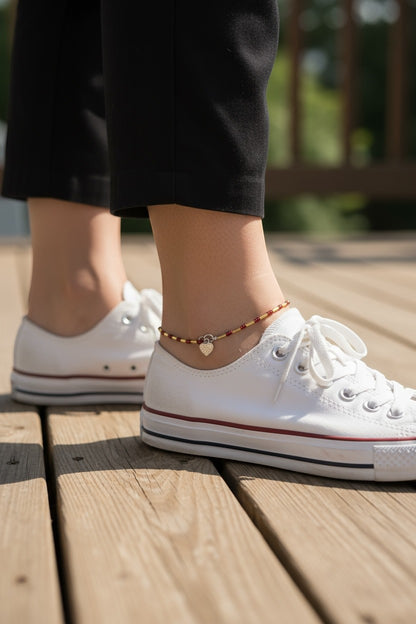 Jena Jewelry handmade seed bead anklet with red beads, gold accents, and a heart charm, worn with white sneakers.