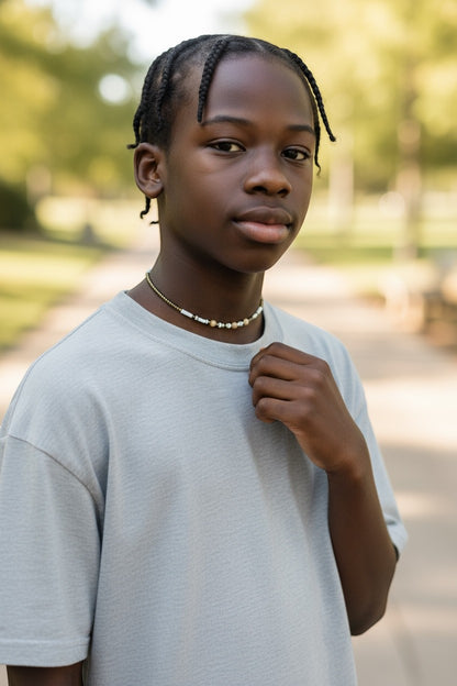 Jena Jewelry handcrafted seed bead necklace with white, brown, and metallic beads on a young person wearing a light blue t-shirt.