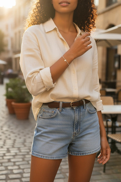 Jena Jewelry small silver heart charm bracelet on a woman's wrist, styled with a cream linen shirt and denim shorts.