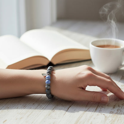 Jena Jewelry sodalite, hematite, and lava stone stretch bracelet with silver charm on a wrist.