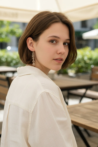 Jena Jewelry stacked drop earrings with smooth, light brown stones and silver-tone wire wrapping. Model wears a cream shirt.