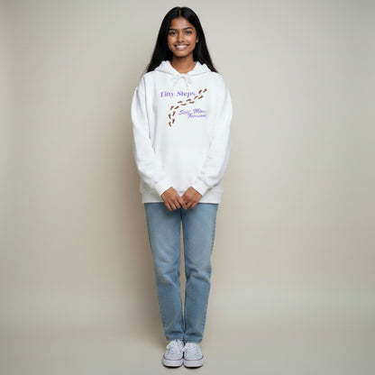 Jena Jewelry white cotton-poly blend hoodie with "Tiny Steps" graphic and kangaroo pocket. Model wears light wash jeans.