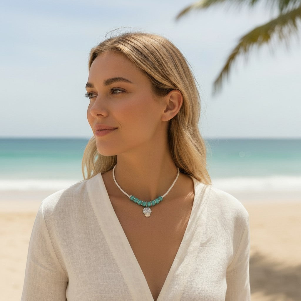 Jena Jewelry turquoise and white seed bead necklace with seashell charm, worn by a woman on a beach.