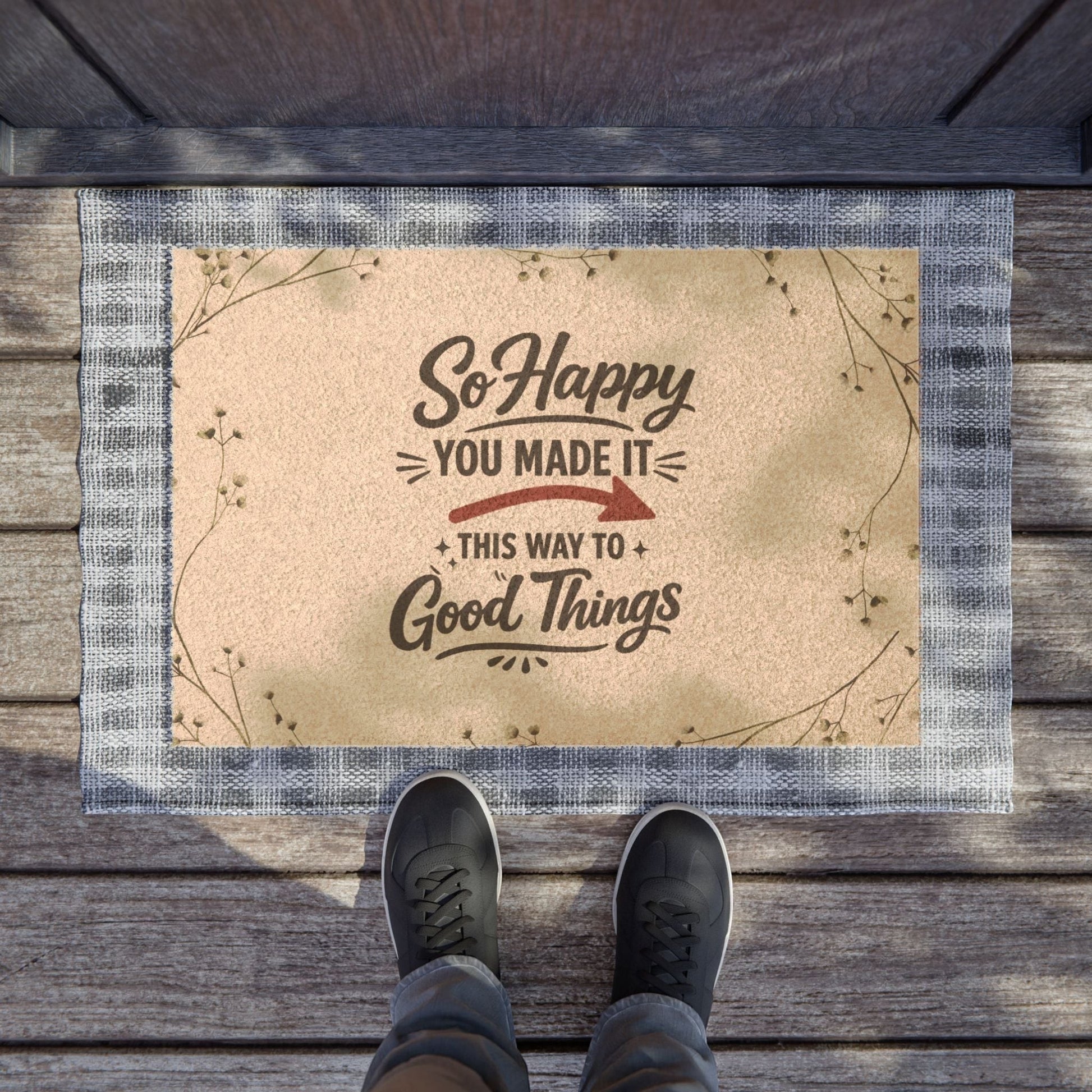 Jena Jewelry "So Happy You Made It" doormat with a beige coir surface, dark text, and a blue checkered border. Features botanical accents.