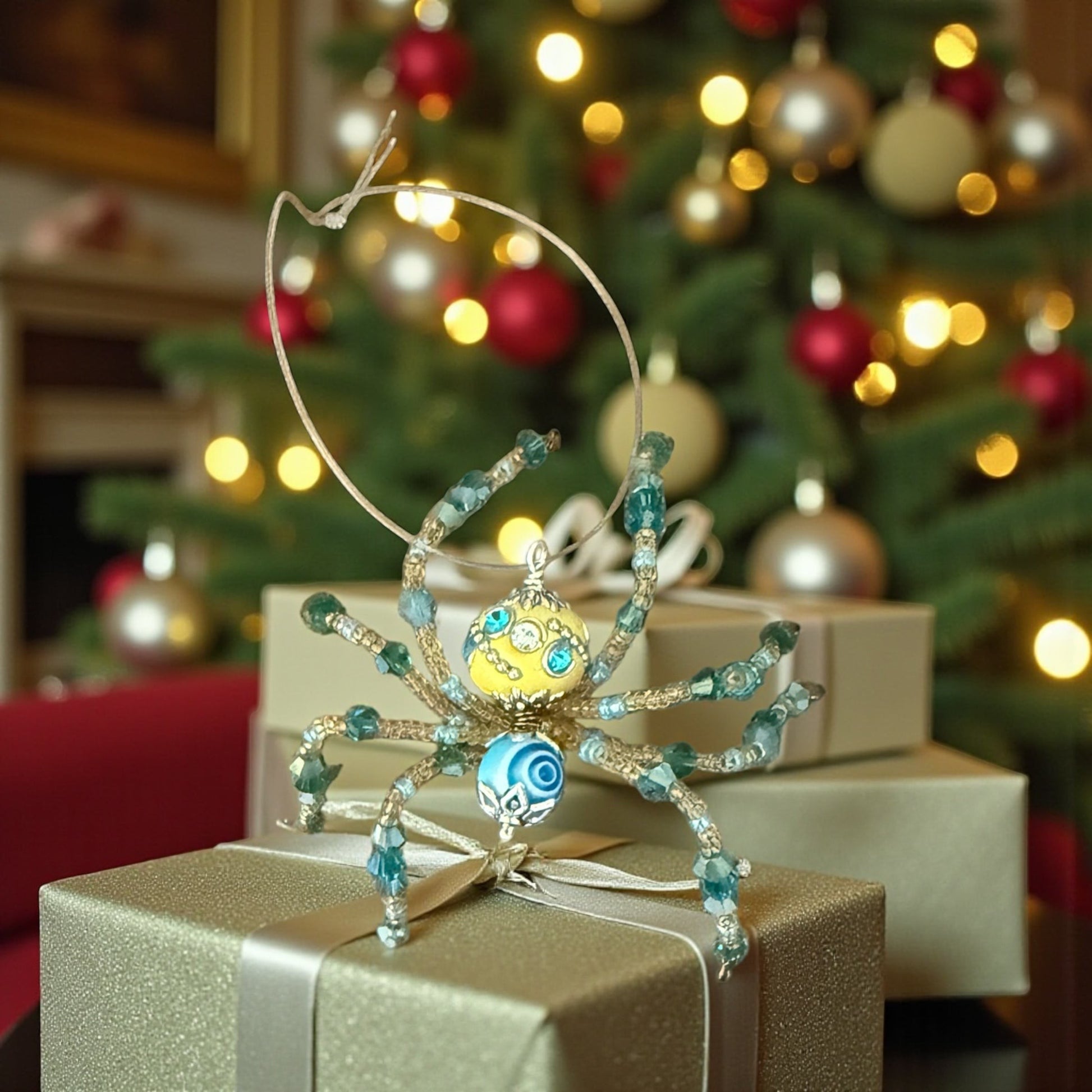 Jena Jewelry handcrafted Christmas spider ornament with yellow and blue beads, silver wire legs, and a blue swirl detail on its body.