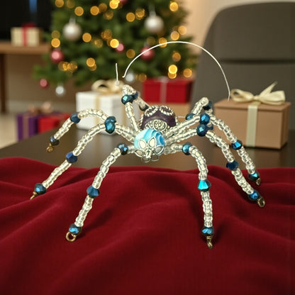 Jena Jewelry handcrafted spider ornament with blue and silver beads, inspired by a Christmas legend. Festive holiday background.