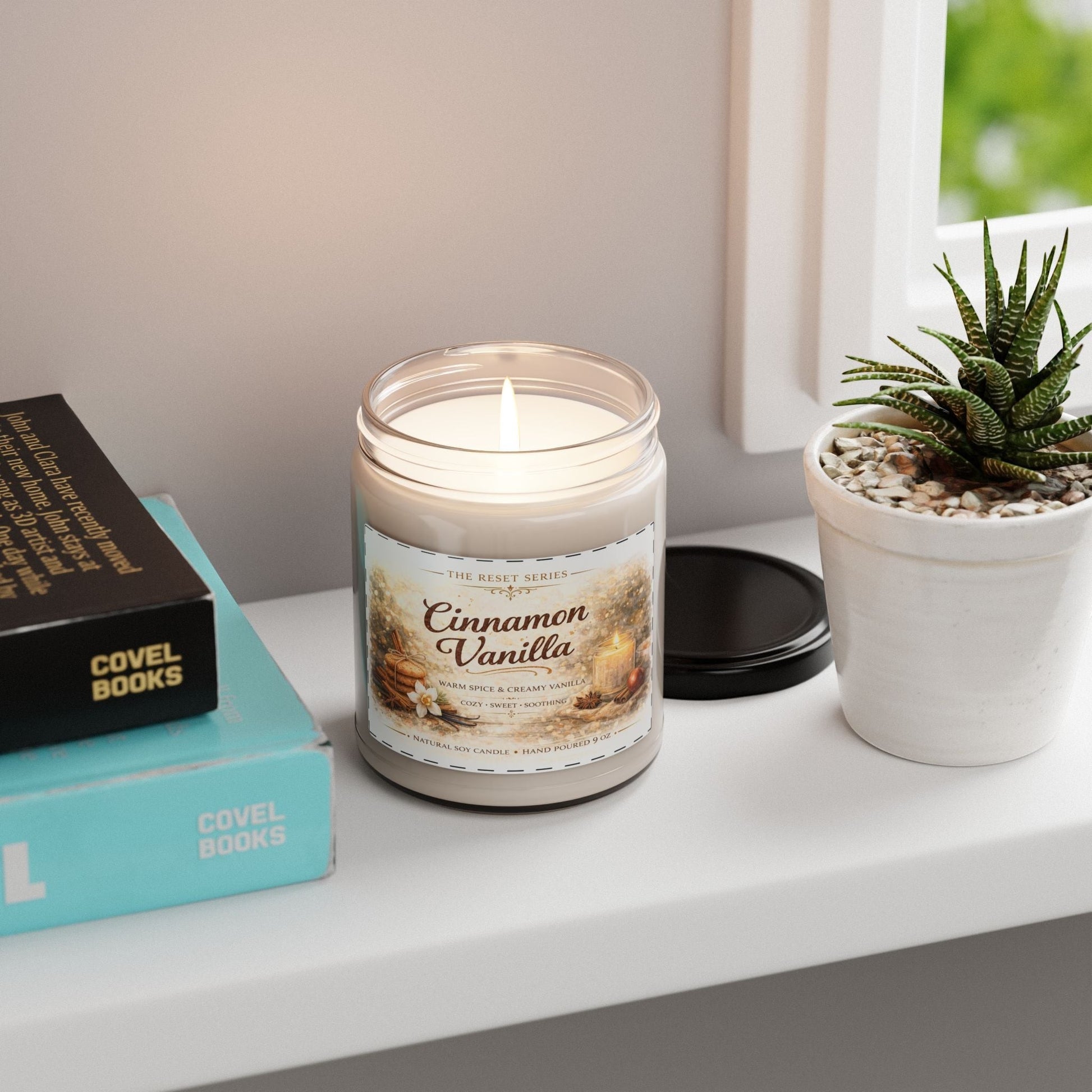Jena Jewelry Cinnamon Vanilla soy candle in a glass jar with a black lid, emitting a warm glow. Cozy fall home fragrance.