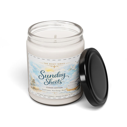 Jena Jewelry Clean Cotton scented soy candle in a reusable glass jar with a black lid, featuring a label with a sky scene and stacked linens.