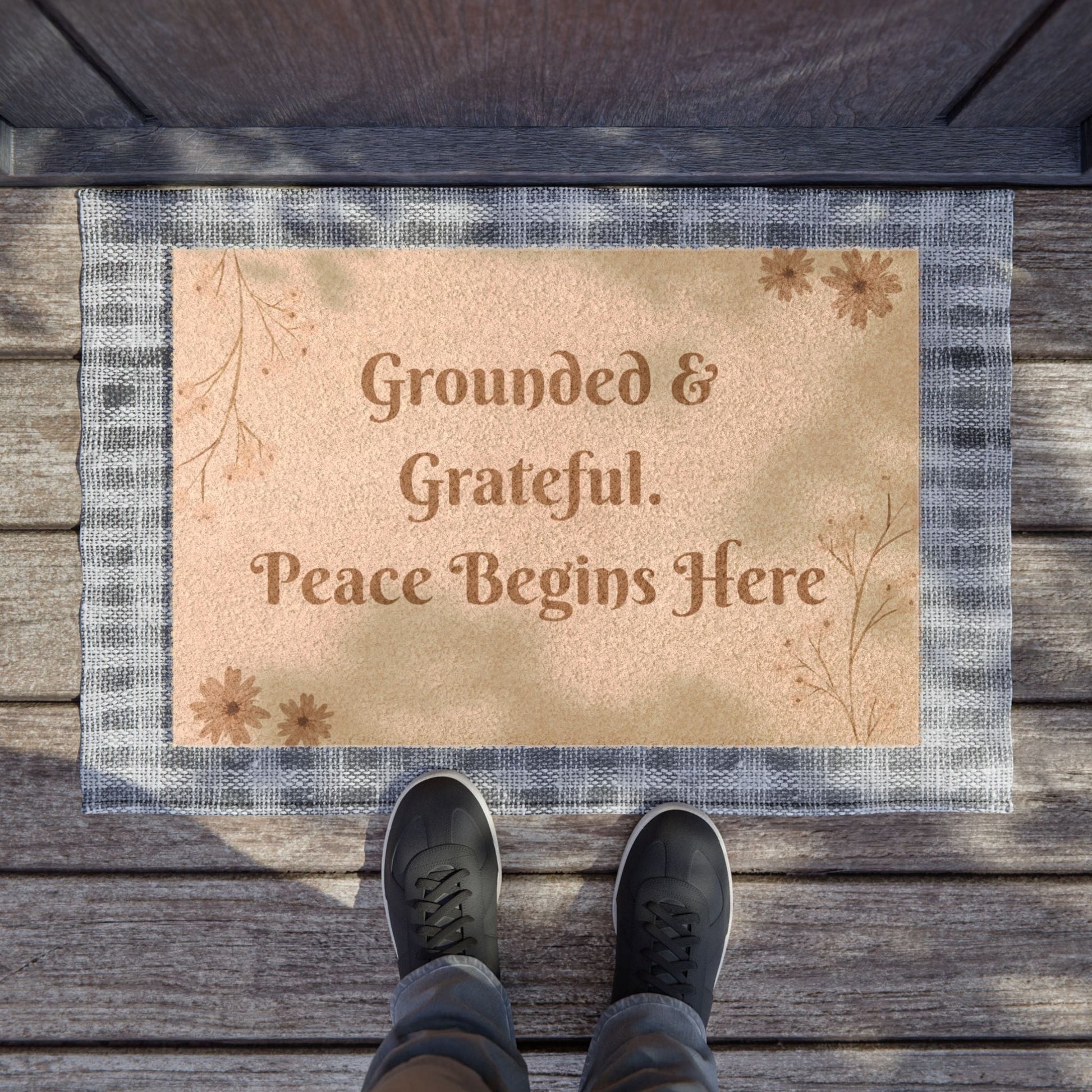 Jena Jewelry "Grounded & Grateful" doormat with a beige center and plaid border. Features text and floral accents.