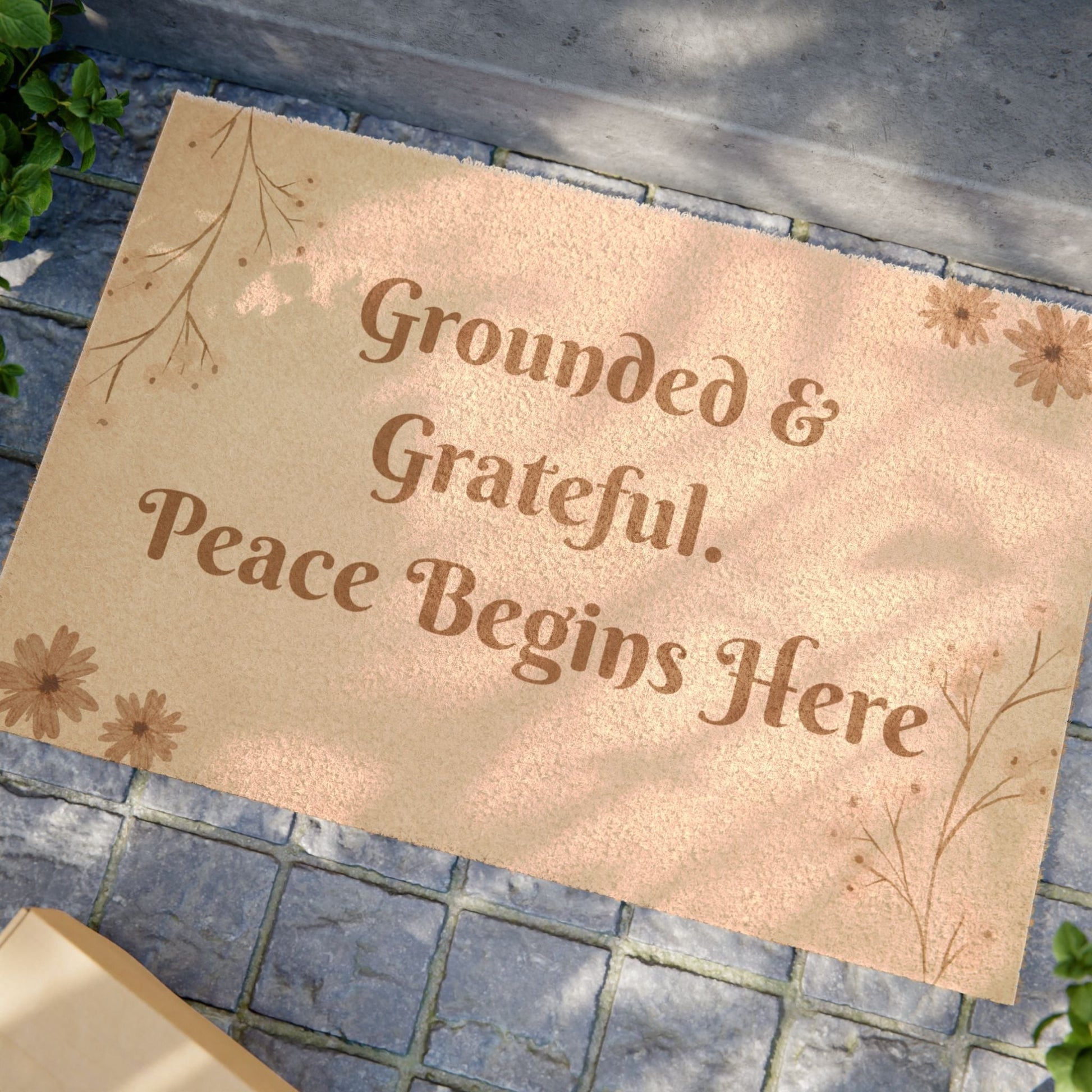 Jena Jewelry tan coir doormat with brown text "Grounded & Grateful. Peace Begins Here" and floral accents.