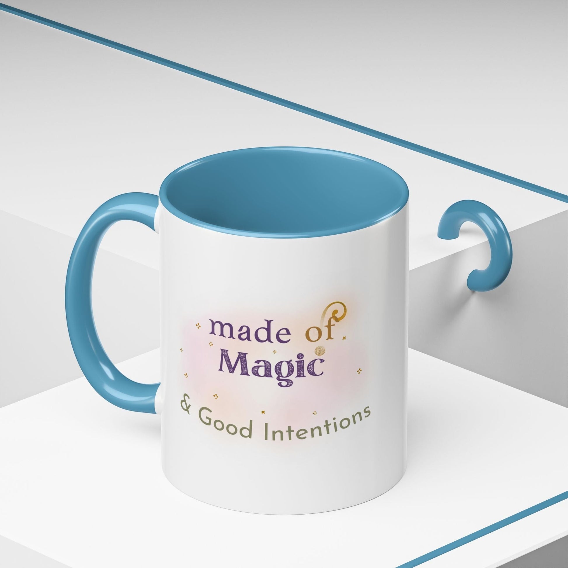 Jena Jewelry white ceramic mug with blue interior and handle, featuring "made of Magic & Good Intentions" text and watercolor design.
