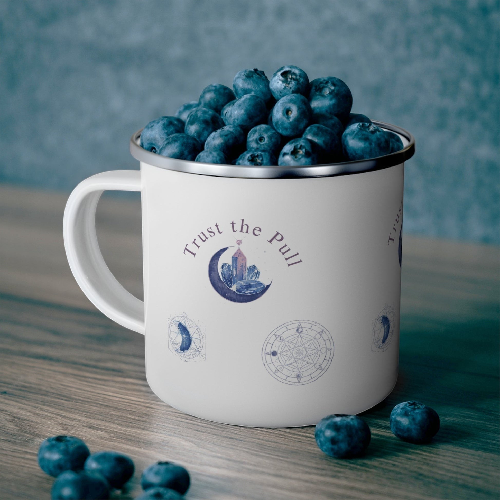 Jena Jewelry white enamel camping mug with moon phase and crystal design, filled with blueberries.