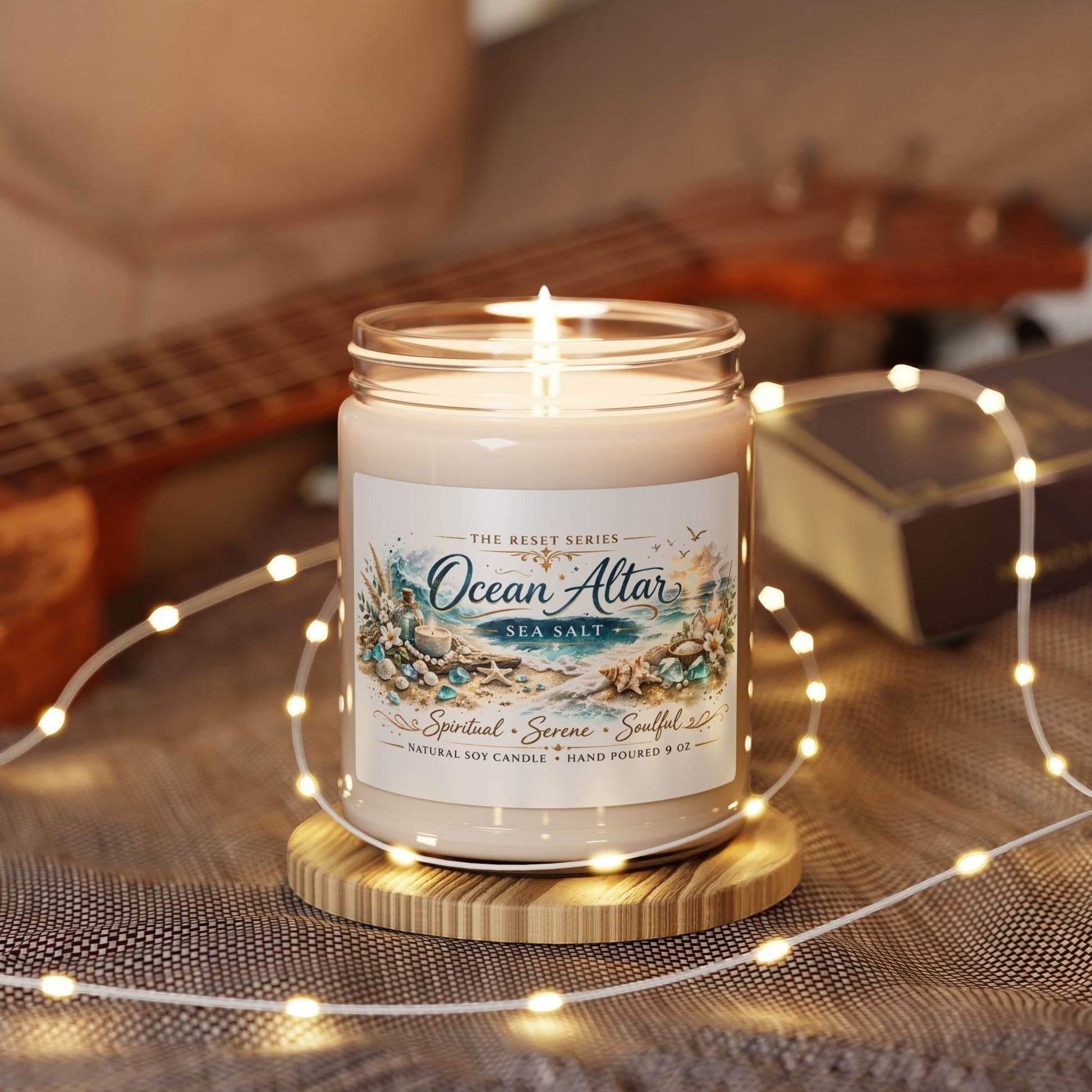 Jena Jewelry Ocean Altar sea salt soy candle with a coastal beach design, lit and on a wooden coaster, surrounded by fairy lights.