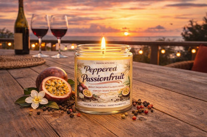Jena Jewelry Peppered Passionfruit natural soy candle with a lit wick, set on a wooden table with passionfruit and peppercorns.