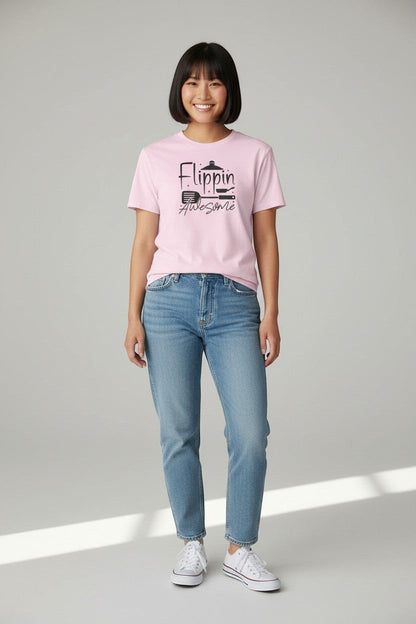 Jena Jewelry pink 100% cotton t-shirt with "Flippin' Awesome" graphic and kitchen icons. Model wears jeans and white sneakers.