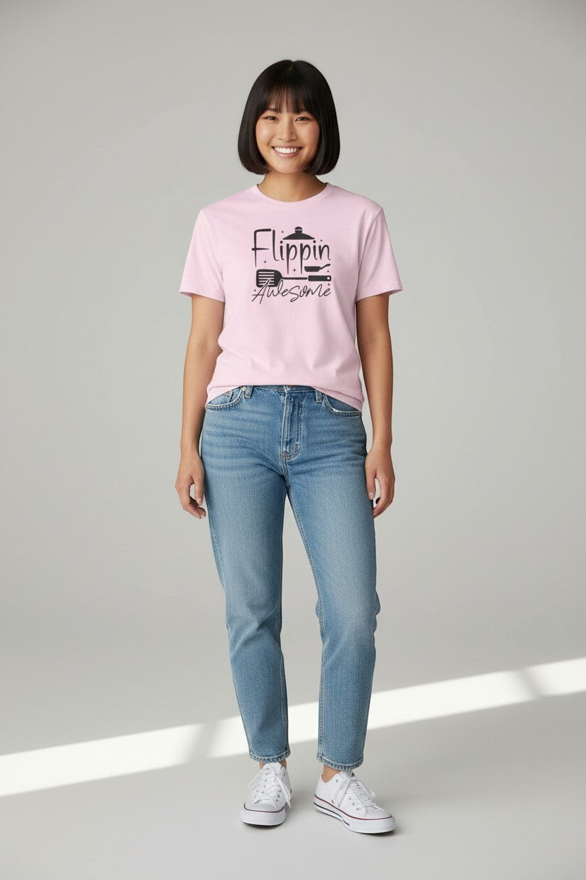 Jena Jewelry pink 100% cotton t-shirt with "Flippin' Awesome" graphic and kitchen icons. Model wears jeans and white sneakers.