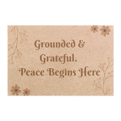 Jena Jewelry beige coir doormat with "Grounded & Grateful. Peace Begins Here" text and floral accents.