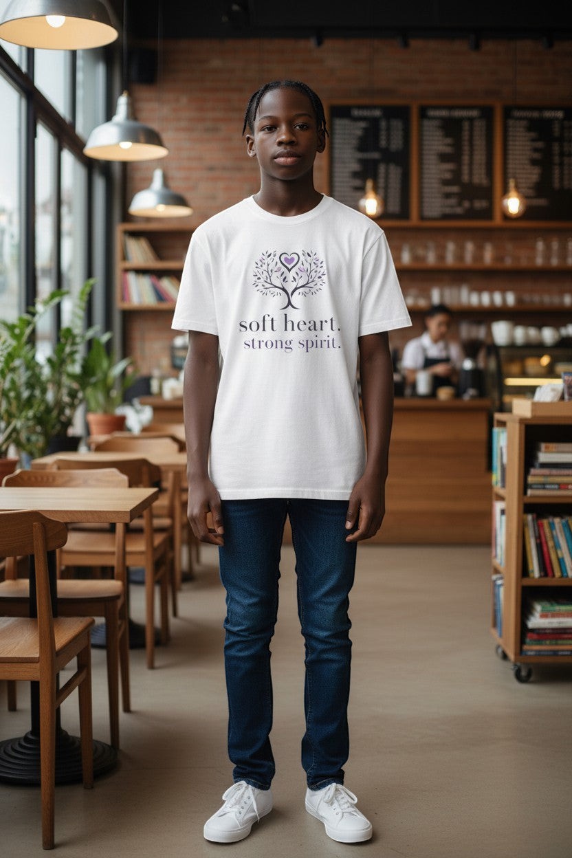 Person wearing white “Soft Heart Strong Spirit” t-shirt in a café setting, a relaxed and uplifting everyday outfit.