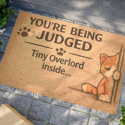 Close-up angled view of “You’re Being Judged” cat welcome mat, highlighting playful design and humorous message.