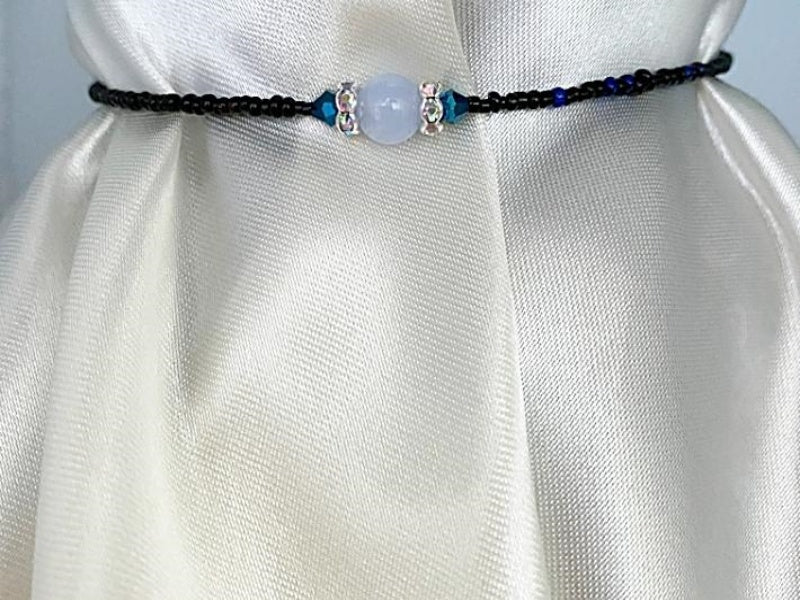Necklace with small black seed beads with small blue and red seed beads mixed in and accented with dark blue glass beads, clear glass rondels, and blue lace agate beads. This is finished with a base metal clasp.