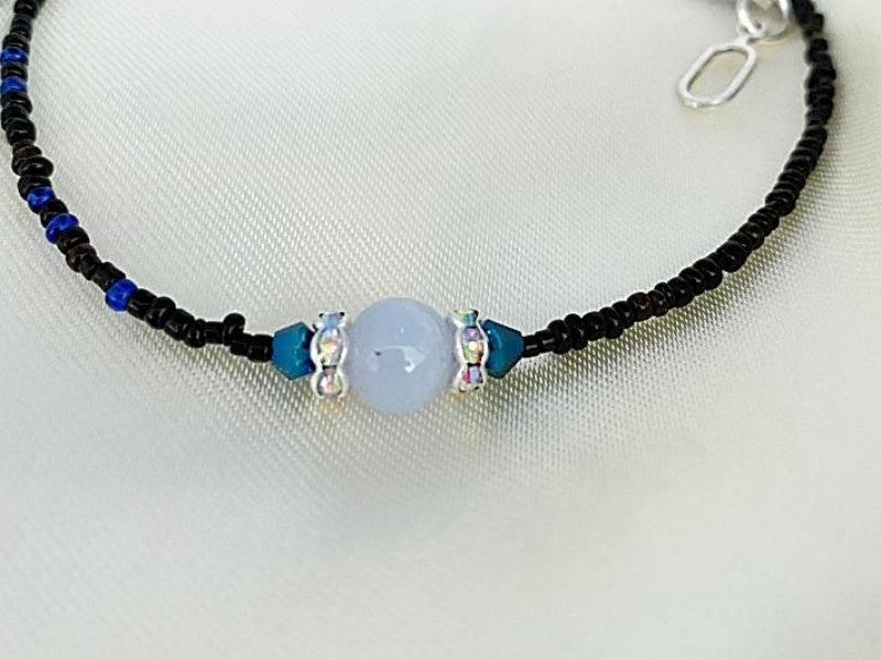 Necklace with small black seed beads with small blue and red seed beads mixed in and accented with dark blue glass beads, clear glass rondels, and blue lace agate beads. This is finished with a base metal clasp.