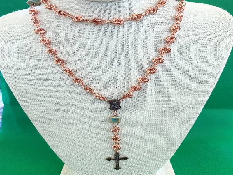 Necklace with copper love knots, square green porcelain beads, copper medallion, and cross on a neck