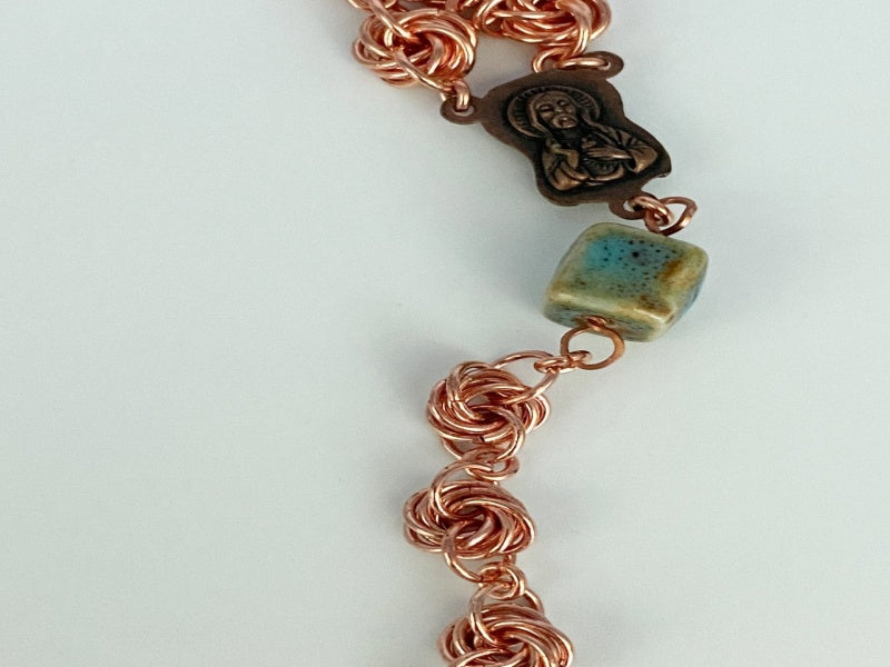 Necklace with copper love knots, square green porcelain beads, copper medallion, and cross.
