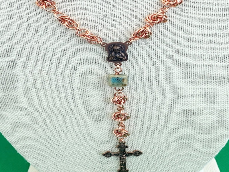 Necklace with copper love knots, square green porcelain beads, copper medallion, and cross.